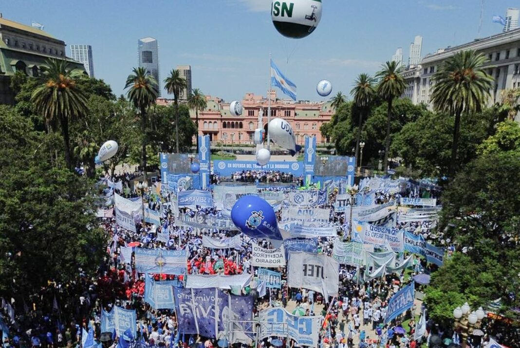 Personas con banderas argentinas marchando en Plaza de Mayo durante una movilización sindical
