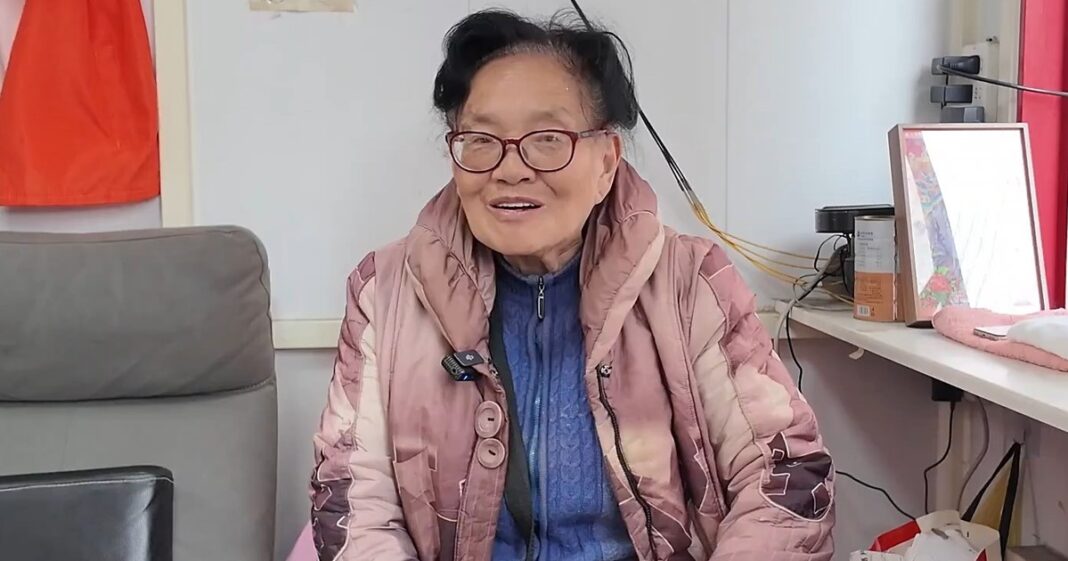 Mujer mayor dentro de una cabina telefónica vidriada en Shanghai