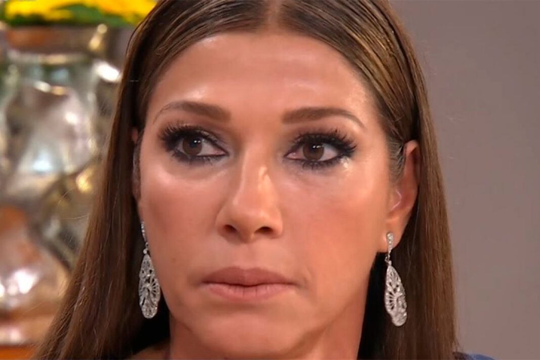 Catherine Fulop sosteniendo un teléfono con la bandera de Venezuela de fondo