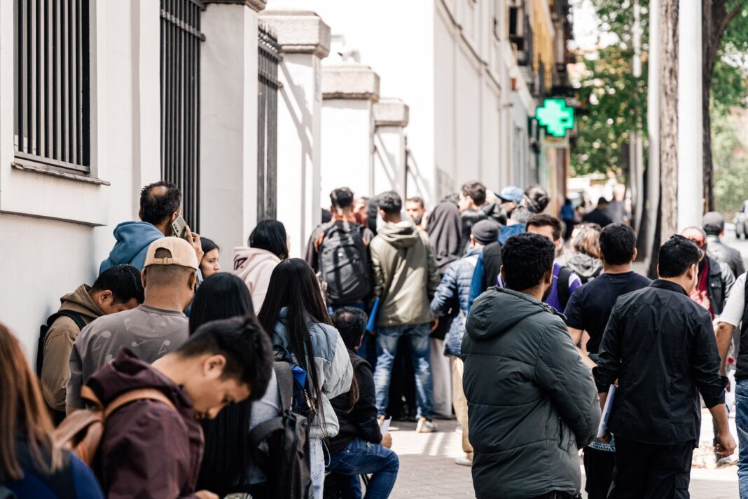 Personas migrantes haciendo fila en una oficina de extranjería en España