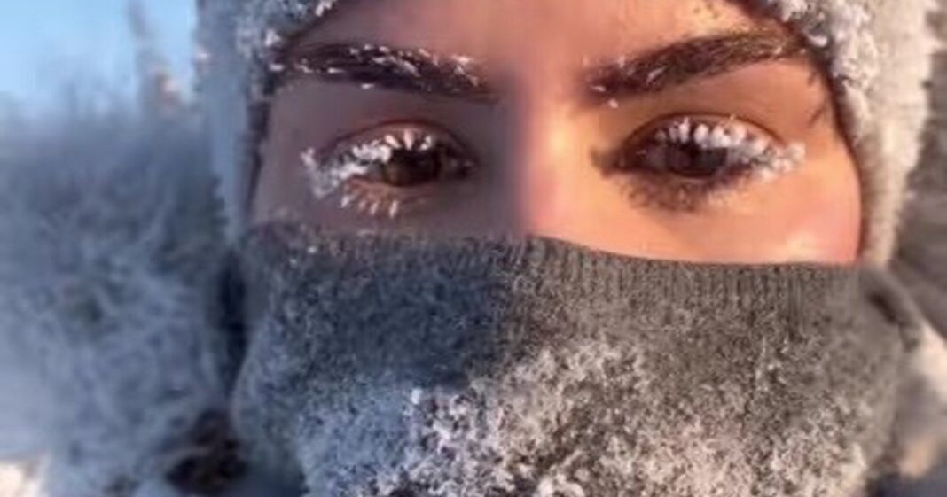 Mujer joven con abrigo de invierno junto a un automóvil en un camino nevado en Yukón, Canadá